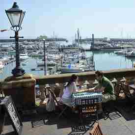 Couple sat at table with checked tablecloth, holding hands next to wall railings overlooking the boats in Ramsgate Royal Harbour