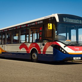 Single decker bus on seafront. White, blue, red and orange areas of colour along side and on front of bus